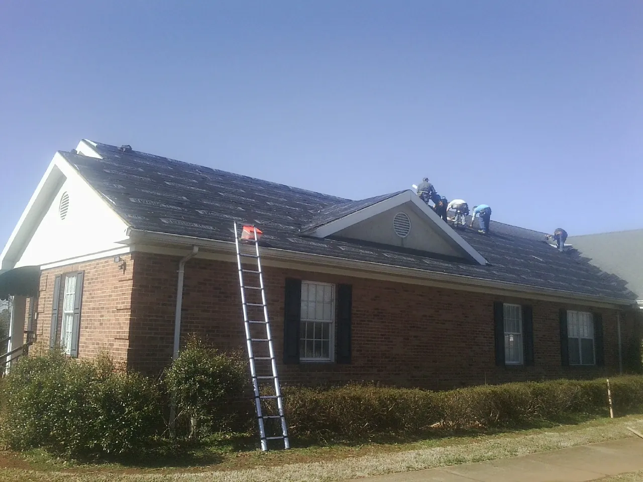 Crew tearing shingles off a brick ranch roof with a ladder set — Metal Roof Repair work by our crew in Philippi