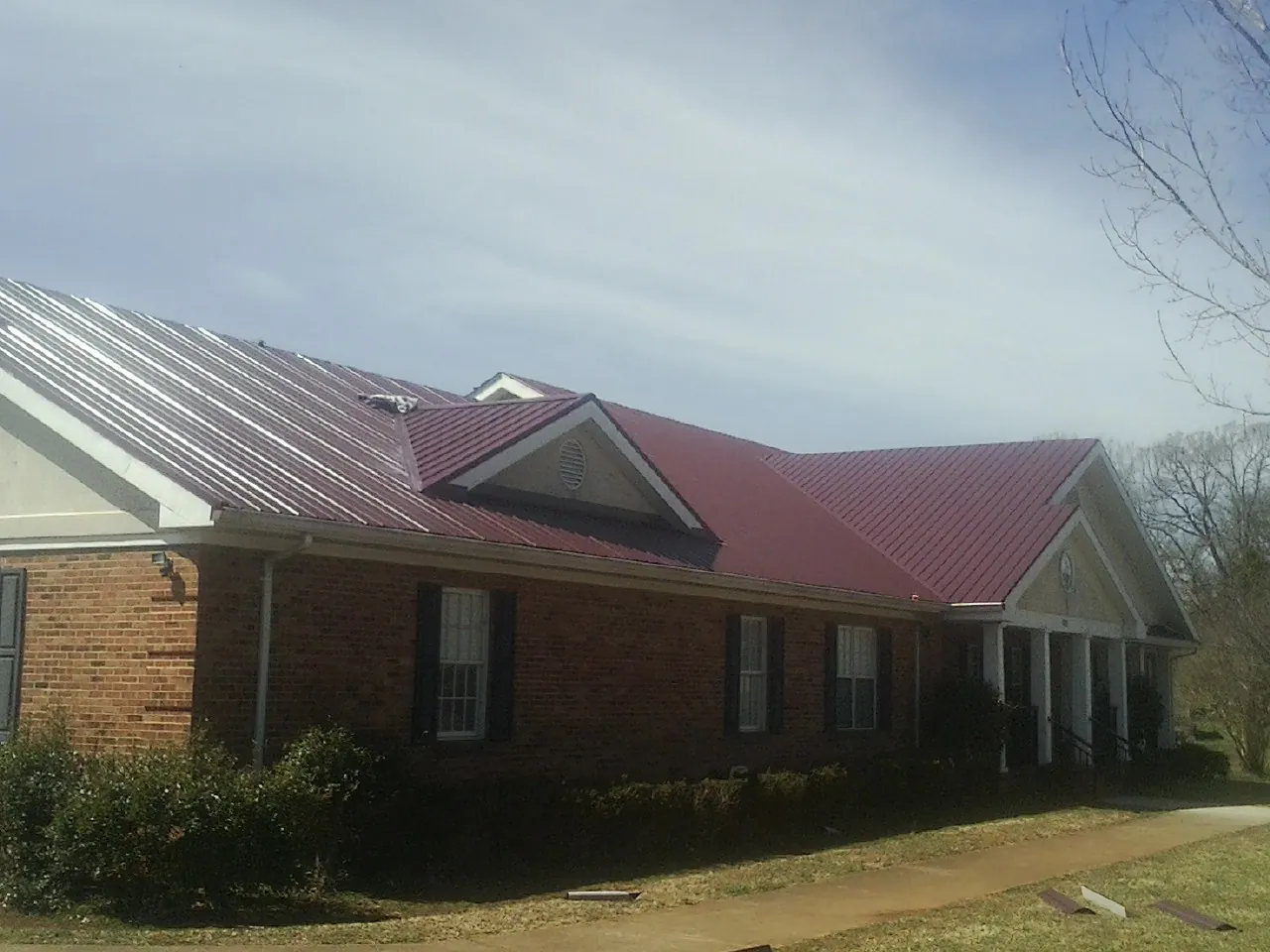 Red metal roof with gabled entries on a long brick building, from a Hail Damage Roof Repair job in Philippi