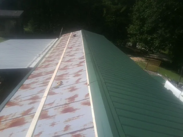 Old rusted panels beside newly installed green metal roofing — Wind Damage Roof Repair by Roofing Brothers in Philippi