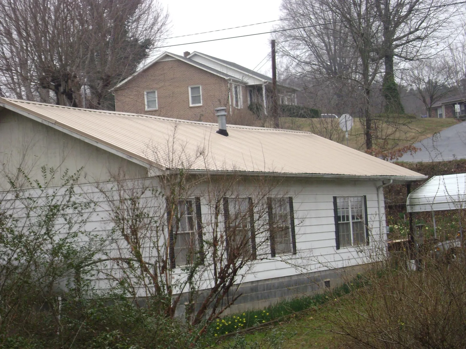 Tan metal roof on a white sided house set into a hillside — Commercial Roofing by Roofing Brothers in Philippi